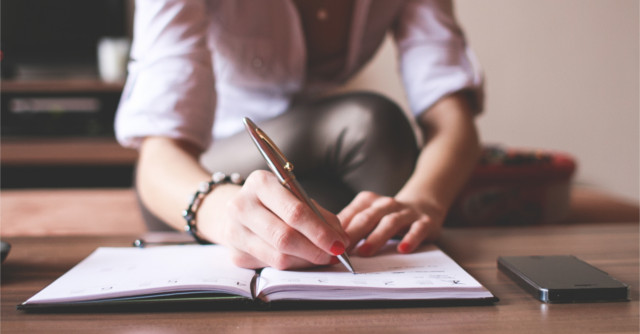 テーブルで上でノートに書き込みをする女性